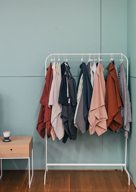 clothes hanging on a stand placed beside a stool with a cup on the top